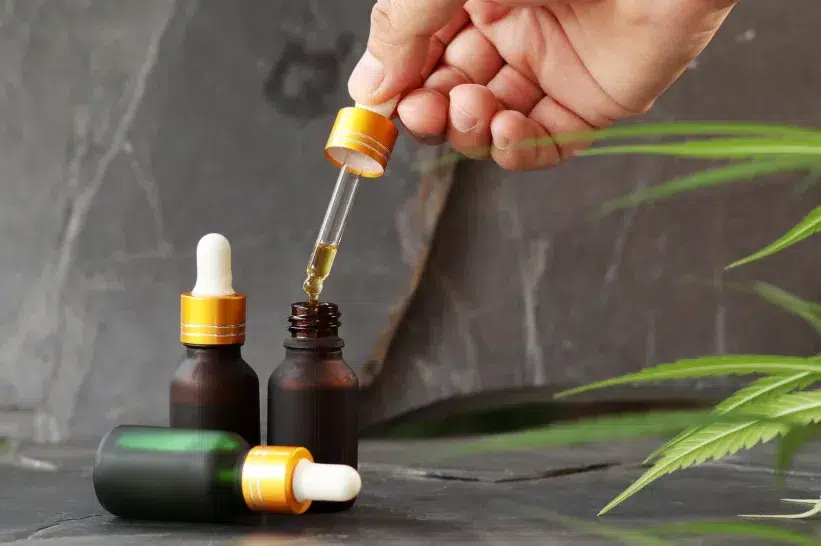 a hand holding a dropper over a small bottle of CBD oil