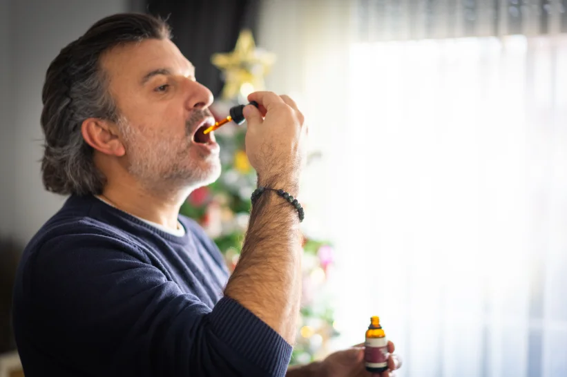 a man with a beard and mustache using a pipette to put a THCA tincture drops in his mouth